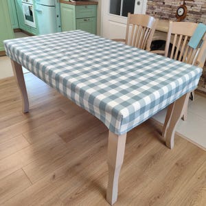 Peut inclure: Une nappe à carreaux bleu clair et blanc couvre une table en bois à quatre pieds. La nappe a un design simple et classique et est parfaite pour ajouter une touche d'élégance à n'importe quelle salle à manger.