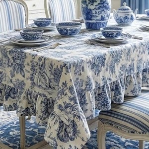 Könnte beinhalten: Ein Esstisch mit einer blau-weißen Blumendecke, passenden Servietten und Geschirr. Der Tisch ist mit Tellern, Schalen und Besteck gedeckt. Eine große Vase und eine Teekanne stehen ebenfalls auf dem Tisch. Die Stühle haben blau-weiß gestreifte Polster.