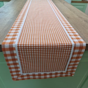 Pode incluir: Um corredor de mesa xadrez laranja e branco com uma borda branca. O corredor é feito de um tecido macio e tecido com um brilho sutil.