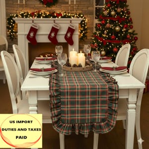 Pode incluir: Uma mesa de jantar de Natal festiva. Uma mesa branca é decorada com pratos, copos e um corredor xadrez com borda com babados. Velas acesas e pinhas estão no centro. Uma árvore de Natal e meias estão no fundo.