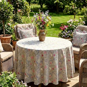 Pode incluir: Uma mesa redonda coberta com uma toalha de cor clara com um delicado padrão floral em tons de rosa, azul e verde. Um vaso de cerâmica cheio com um colorido buquê de flores silvestres está posicionado no centro da mesa.