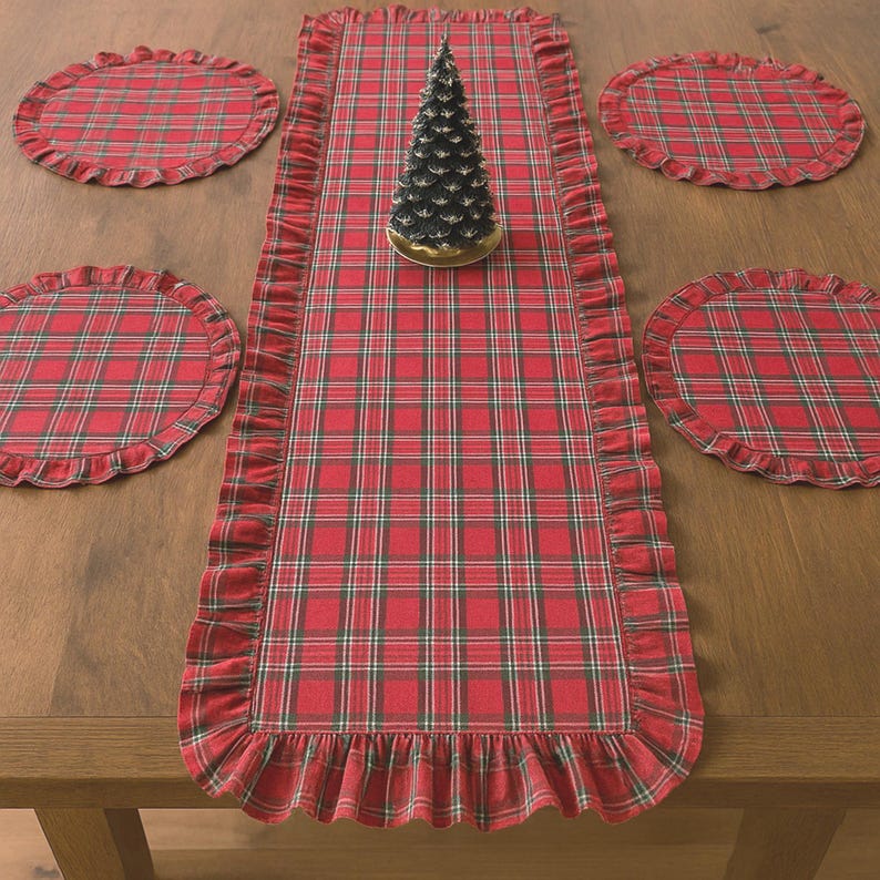 Pode incluir: Um caminho de mesa retangular e quatro jogos americanos circulares com um padr&atilde;o xadrez vermelho, verde e branco com bordas franzidas. Um pequeno ornamento decorativo de &aacute;rvore em forma de cone verde escuro est&aacute; no centro do caminho.