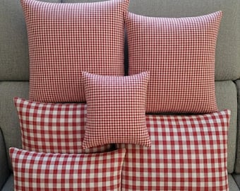 May include: A collection of red and white checkered throw pillows in various sizes, arranged on a gray sofa. The pillows have a classic gingham pattern, creating a cozy and inviting aesthetic. The arrangement includes square and rectangular shapes.