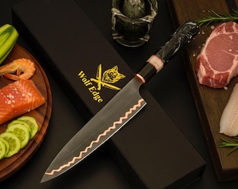 May include: A chef knife with a dark blade featuring a wavy copper-colored edge and a black marbled handle, resting on a black box labeled Wolf Edge with a gold wolf logo. The knife is surrounded by raw salmon, shrimp, cucumber, and meat.