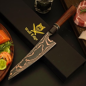May include: A kitchen knife with a dark, wavy patterned blade and a brown wooden handle. The blade features a sharp point and a curved edge. It rests on a black rectangular box with the gold text Wolf Edge and a wolf head logo printed on it.