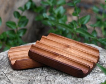 May include: Two wooden soap dishes with a grooved design. The dishes are made of natural wood and have a light brown color.