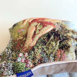 May include: A tapestry pillow with a colorful floral design and a nude figure. The pillow has a beige backing and a blue label that says "VEDUARTE".