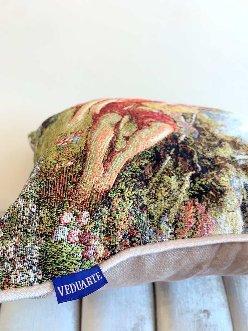 May include: A tapestry pillow with a colorful floral design and a nude figure. The pillow has a beige backing and a blue label that says "VEDUARTE".