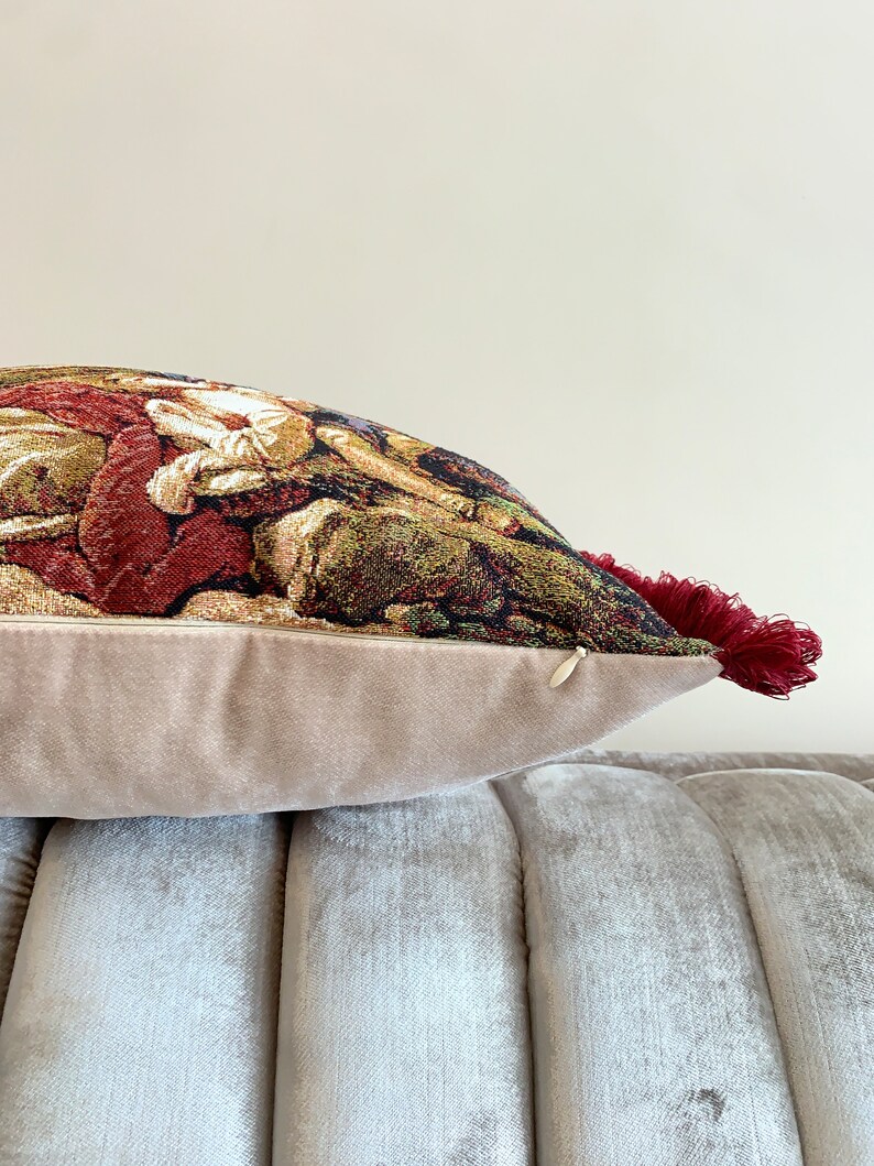 Op de afbeelding: Een decoratief kussen met een tapijt-achtige stof met een kleurrijk bloemenpatroon. Het kussen heeft een beige fluwelen achterkant en een rode kwast.