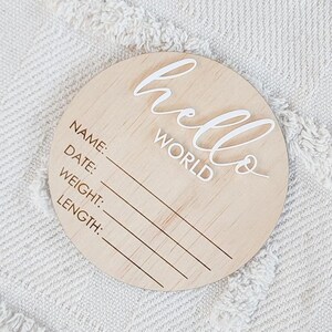 May include: A round wooden plaque with the text "hello world" in white cursive lettering. The plaque has blank lines for "name", "date", "weight", and "length".