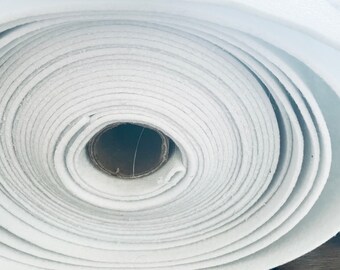 May include: A roll of white fabric, tightly wound, revealing concentric circles. The fabric appears to be a soft, possibly felt-like material. The core of the roll is a brown cardboard tube. The image is a close-up, highlighting the texture and layers.