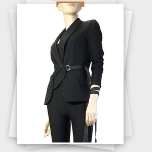 May include: Black blazer with a notched lapel, a matching belt with a silver buckle, and long sleeves. The blazer is paired with black pants. The outfit is displayed on a mannequin.