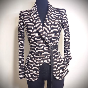May include: A black and white patterned blazer with a belt. The blazer has a unique design with a wrap-style front and long sleeves. The belt cinches the waist, creating a fitted silhouette. The pattern is a repeating geometric design.