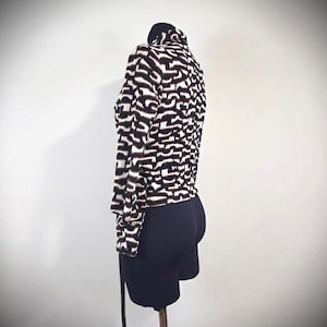 May include: A black and white patterned jacket with a high collar. The jacket has a unique abstract design and long sleeves. The jacket is paired with black shorts. The jacket is displayed on a mannequin.