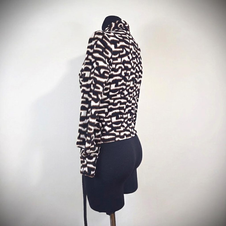 May include: A black and white patterned jacket with a high collar. The jacket has a unique abstract design and long sleeves. The jacket is paired with black shorts. The jacket is displayed on a mannequin.