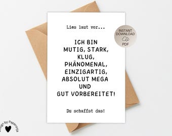 May include: A white card with black text, resting on a brown envelope. The card reads "Lies laut vor... ICH BIN MUTIG, STARK, KLUG, PHÄNOMENAL, EINZIGARTIG, ABSOLUT MEGA UND GUT VORBEREITET! Du schaffst das!" with a PDF download icon.