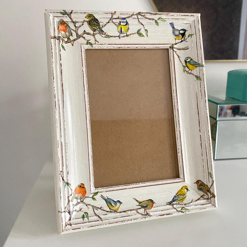 May include: White picture frame with a distressed finish and a brown mat. The frame is decorated with a border of small birds on branches.