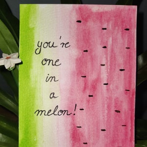 May include: Watercolor greeting card with a watermelon design. The card features a green and pink gradient, black seed details, and the handwritten text "you're one in a melon!".
