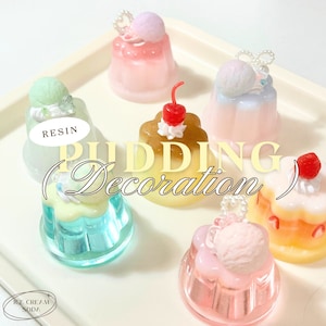 May include: An assortment of six miniature resin pudding desserts with various toppings, including cherries, ice cream, and whipped cream. The puddings are displayed on a white tray with the text "PUDDING (Decoration)" in the centre.