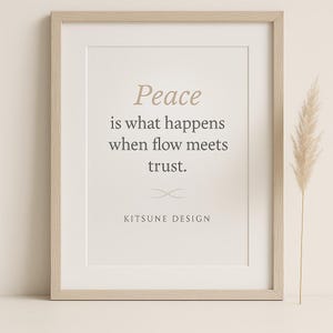 May include: A framed print with the quote "Peace is what happens when flow meets trust." in a serif font. The print is in a light wood frame and features the "Kitsune Design" logo. A decorative plant is to the right of the frame.
