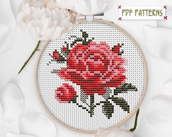 May include: A cross-stitch pattern of a red rose in a wooden embroidery hoop. The rose has varying shades of red and pink, with green leaves and stems. The text "PDF PATTERNS" is in the upper right corner. White flowers and petals are in the background.