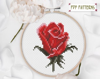 May include: A red rose cross-stitch pattern in a wooden embroidery hoop. The rose is a single bloom with green leaves and a stem.