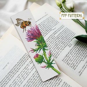 May include: Cross stitch pattern for a bookmark featuring a bee and a thistle flower. The pattern is in shades of green, purple, pink, and yellow. The bookmark is ideal for adding a touch of nature to your reading.