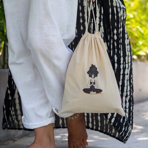 Puede incluir: Una bolsa de cord&oacute;n blanco con una ilustraci&oacute;n en blanco y negro de una persona meditando con un cielo estrellado sobre su cabeza. La bolsa est&aacute; hecha de algod&oacute;n natural y tiene un dise&ntilde;o simple.