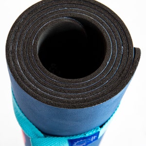 Puede incluir: Una esterilla de yoga azul enrollada con una superficie de goma negra y una correa turquesa con texto blanco.