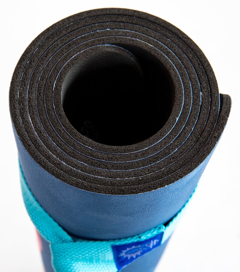Puede incluir: Una esterilla de yoga azul enrollada con una superficie de goma negra y una correa turquesa con texto blanco.