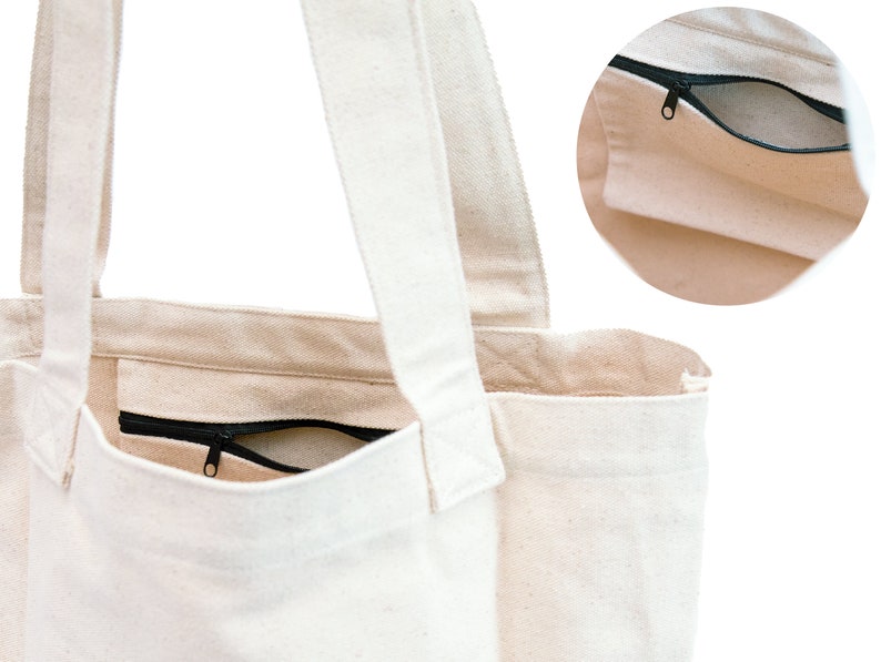 Puede incluir: Una bolsa de lona blanca con un bolsillo con cremallera en la parte delantera. La bolsa tiene dos asas largas para llevar.