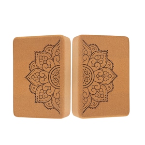 Peut inclure: Deux blocs de yoga rectangulaires en liège brun clair. Chaque bloc présente un motif mandala symétrique brun foncé sur un côté. Les blocs sont placés côte à côte, contre un fond noir. Ces blocs sont utilisés pour le yoga et l'étirement.