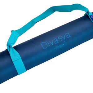 Puede incluir: Una esterilla de yoga azul con una correa de transporte turquesa. La esterilla tiene el texto "Divasya Yoga" impreso en ella.