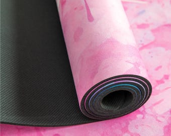 Puede incluir: Una esterilla de yoga rosa con un diseño similar a la acuarela. La esterilla está enrollada y tiene una parte inferior antideslizante negra.