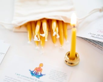 May include: A lit yellow candle in a gold holder, with a bag of yellow candles. The image includes printed cards with text and a graphic of a person meditating. The theme is related to meditation and mindfulness.
