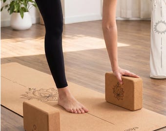 May include: A yoga scene featuring a natural cork yoga mat with a lotus flower design and two rectangular cork yoga blocks. The mat and blocks are light brown. The mat has the word "Divasya" printed on it.