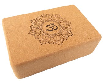 May include: A brown cork yoga block with an engraved mandala design and the symbol "Om" in the center.