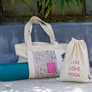 Puede incluir: Dos bolsas de lona blancas con texto rosa. Una bolsa tiene el texto "Life is better with yoga" y la otra bolsa tiene el texto "Live Love Yoga". Una esterilla de yoga azul verdoso est&aacute; delante de las bolsas.