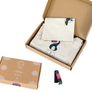 Puede incluir: Una caja de cart&oacute;n marr&oacute;n con una bolsa de yoga blanca en su interior. La bolsa tiene una ilustraci&oacute;n en blanco y negro de una mujer meditando. La caja est&aacute; etiquetada con "Yoga Bag".