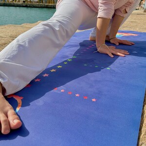 Puede incluir: Una persona haciendo una pose de yoga en una esterilla de yoga azul con estrellas arco&iacute;ris. La esterilla est&aacute; sobre una superficie de hormig&oacute;n.