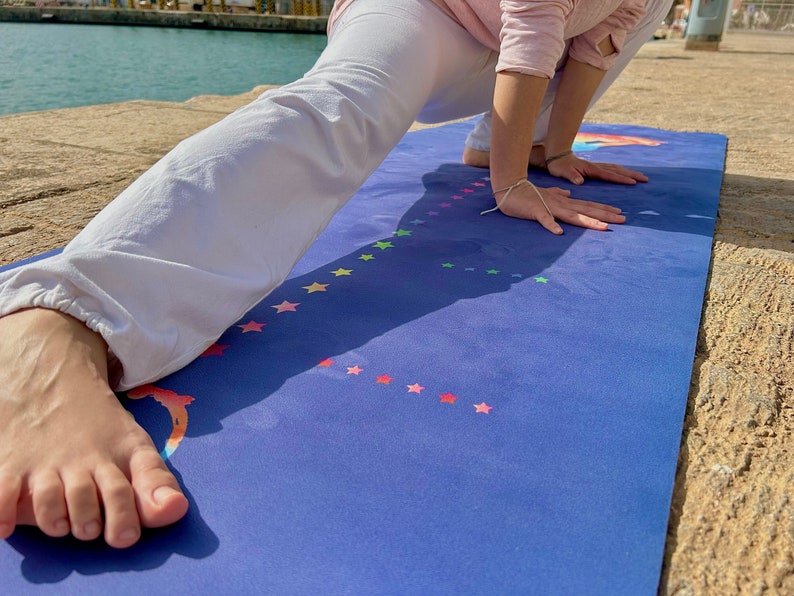 Puede incluir: Una persona haciendo una pose de yoga en una esterilla de yoga azul con estrellas arco&iacute;ris. La esterilla est&aacute; sobre una superficie de hormig&oacute;n.