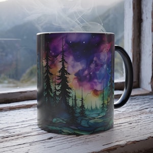 May include: Black coffee mug with a colorful watercolor design of a forest scene with a starry sky. The mug has a black handle.