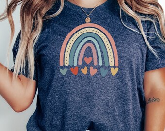 May include: A navy blue t-shirt with a rainbow graphic and small hearts. The rainbow is made up of red, orange, yellow, green, blue, and purple stripes.