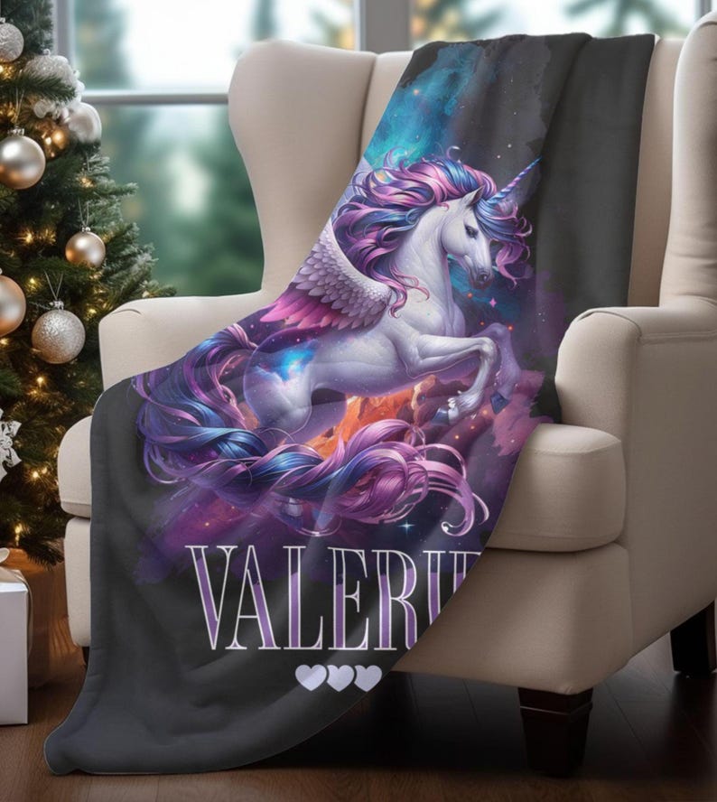 May include: A black blanket draped over a cream-colored armchair. The blanket features a majestic white unicorn with a flowing purple and pink mane and tail, and wings. The name "VALERIE" is printed on the blanket, along with three white hearts.