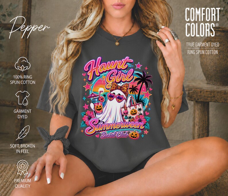 Puede incluir: Una camiseta gris oscuro de manga corta con un estampado gr&aacute;fico de un fantasma con gafas de sol en forma de coraz&oacute;n y un lazo de leopardo. El dise&ntilde;o incluye palmeras, una puesta de sol, flores tropicales y el texto Haunt Girl Summerween Social Club.