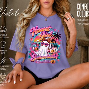 Puede incluir: Una camiseta violeta con un estampado gr&aacute;fico de un fantasma con gafas de sol en forma de coraz&oacute;n y un lazo de leopardo, sosteniendo una bebida y un bolso. El texto dice Haunt Girl Summerween Social Club, rodeado de palmeras y calabazas.