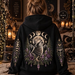 Peut inclure: Un sweat à capuche noir avec un motif détaillé au dos représentant un loup hurlant à la pleine lune, entouré de pins, de fleurs violettes, de cristaux et de phases lunaires. Les manches présentent des motifs verticaux de phases lunaires.