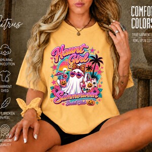 Puede incluir: Una camiseta de color amarillo mostaza con un estampado gr&aacute;fico de un fantasma con gafas de sol en forma de coraz&oacute;n y un lazo de leopardo. El texto dice Haunt Girl Summerween Social Club, junto a palmeras y calabazas.
