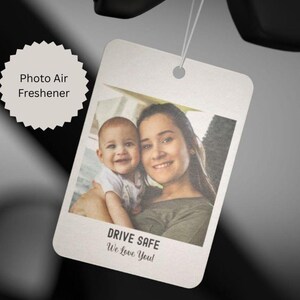 May include: A rectangular photo air freshener with a picture of a woman and a baby. The air freshener has the text "DRIVE SAFE We Love You!" at the bottom. The words "Photo Air Freshener" are in a white starburst shape.
