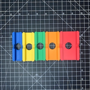 May include: Five colorful plastic track pieces with a hole in the center of each piece. The pieces are blue, yellow, green, orange, and red.